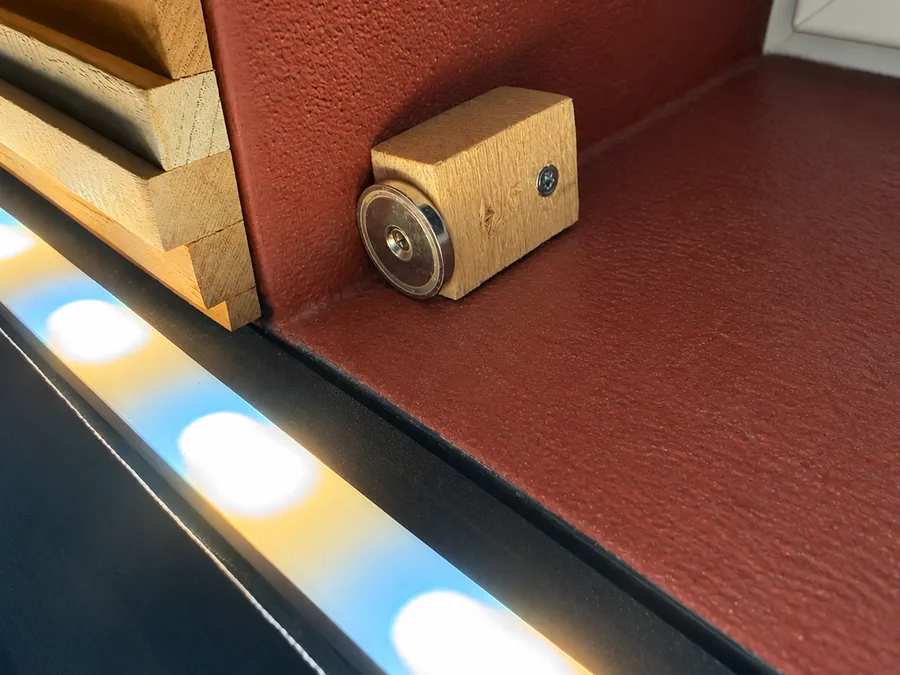 Runder Magnet auf einem Holzklotz in der unteren Fensterlaibung, der die Platte positioniert und hält.