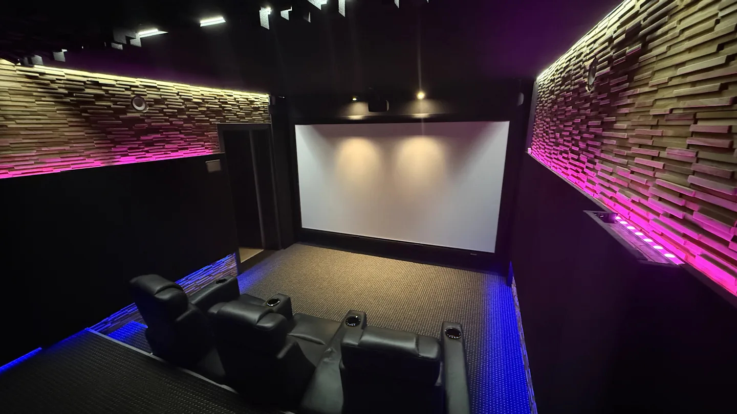 Fertiges Heimkino mit großer leerer Leinwand, drei Sesseln, Holzdiffusoren und indirekter Beleuchtung