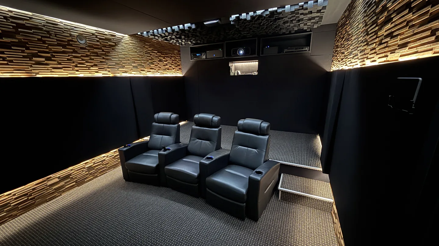 Fertiges Heimkino mit drei schwarzen Sesseln, beleuchteten Holzdiffusoren und integrierter Technikwand