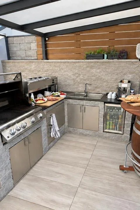 Outdoorküche während eines Brunchs mit geöffnetem Gasgrill, vorbereiteten Speisen, Spüle und Getränkekühlschrank