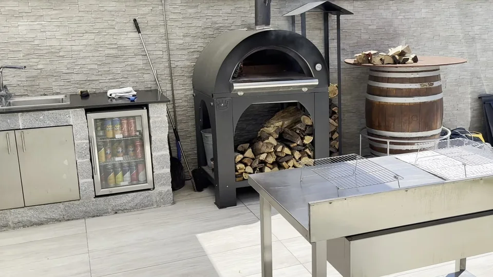 Holzbackofen neben der Outdoorküche mit Edelstahltisch im Vordergrund