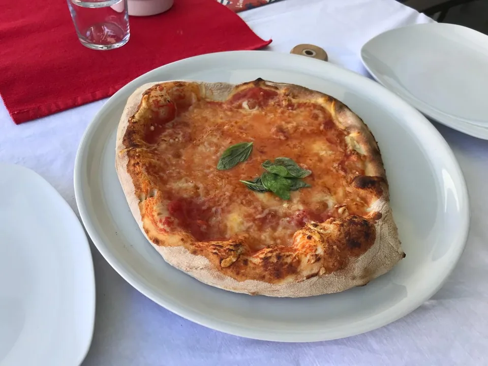 Unregelmäßig geformte Pizza aus meinem ersten Jahr auf einem weißen Teller, belegt mit Tomate, Käse und Basilikum.