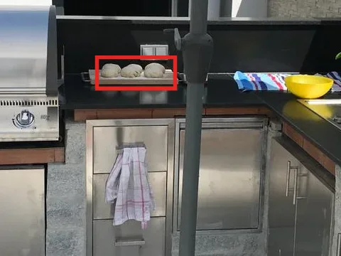Drei ungeschützte Teigballen auf einem Brett in der sonnigen Outdoorküche, mit einem roten Rahmen markiert.
