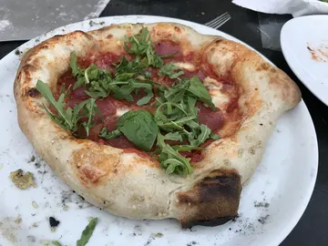 Unregelmäßige Pizza mit Salami und Rucola auf einem weißen Teller.