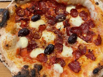 Pizza mit Salami, schwarzen Oliven und gebräuntem Rand.