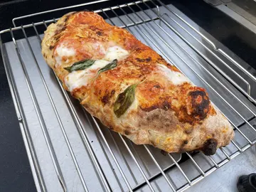 Gebackene Calzone mit Tomate, Käse und Basilikum auf der Außenseite, auf einem Metallgitter.