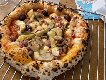 Pizza mit Artischocken, Pilzen, Oliven und hohem gebräuntem Rand auf einem Metallgitter.