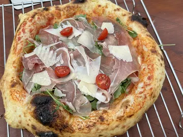 Pizza mit Prosciutto, Rucola, Tomaten und gehobeltem Käse auf einem Abkühlgitter.