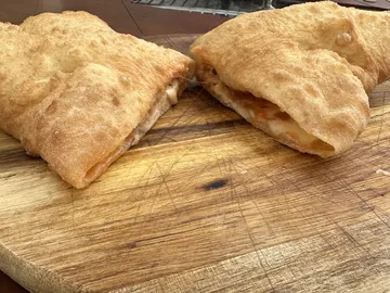 Aufgeschnittene Panzerotta mit goldbrauner Oberfläche und sichtbarer Füllung auf einem Holzbrett.