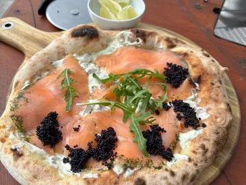 Pizza mit Lachs und Rucola auf einem Holzbrett.