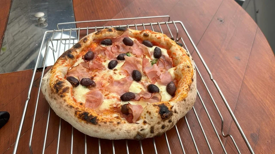 Frisch gebackene Pizza mit Schinken und schwarzen Oliven auf einem Abkühlgitter.