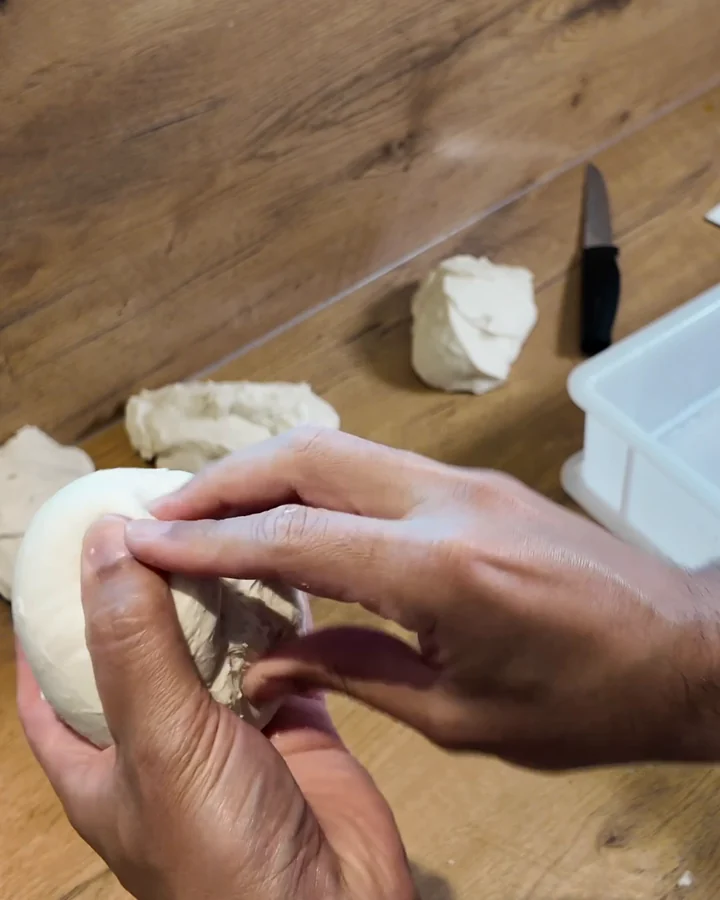 Mario drückt die offene Naht an der Unterseite eines Pizzateigballens mit den Fingern zusammen.